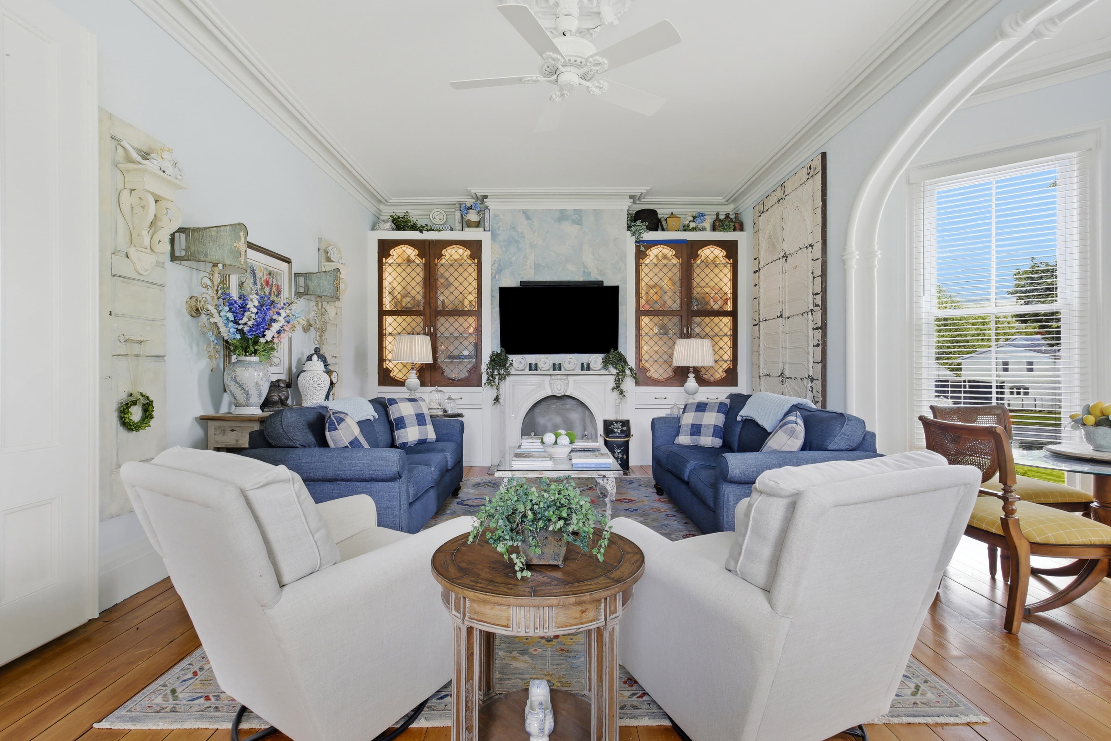 A cozy living room with blue sofas, light-colored armchairs, a central table, and decorative elements against a soft blue wall.