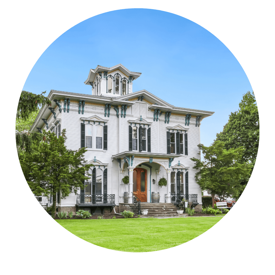 Victorian-style white house with green accents surrounded by greenery.