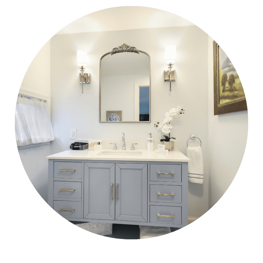 A modern bathroom featuring a light gray vanity, a mirror, and decorative wall sconces with an orchid plant and artwork.